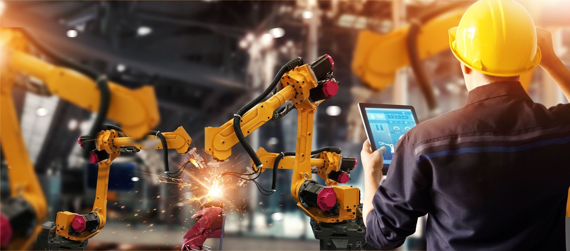An engineer monitoring welding robots from a tablet